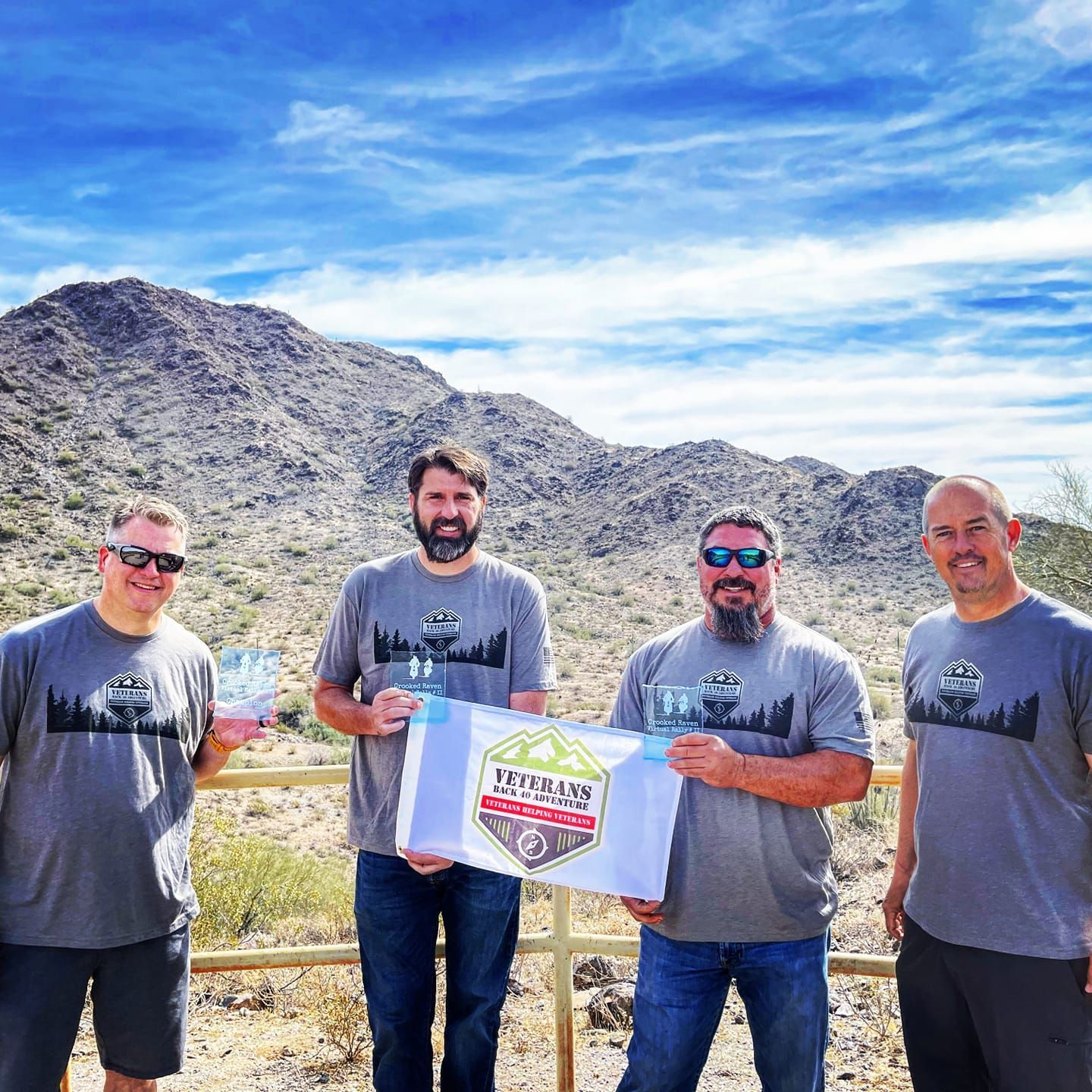 4 men wearing t-shirts and holding up a flag.