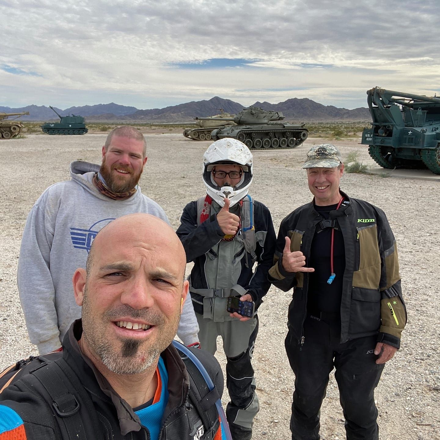 Picture of 4 people smiling for the camera one is wearing a motorcycle helmet.