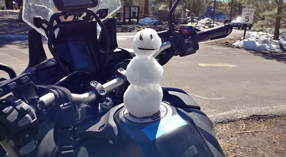 A snowman is sitting on the fuel tank of a motorcycle