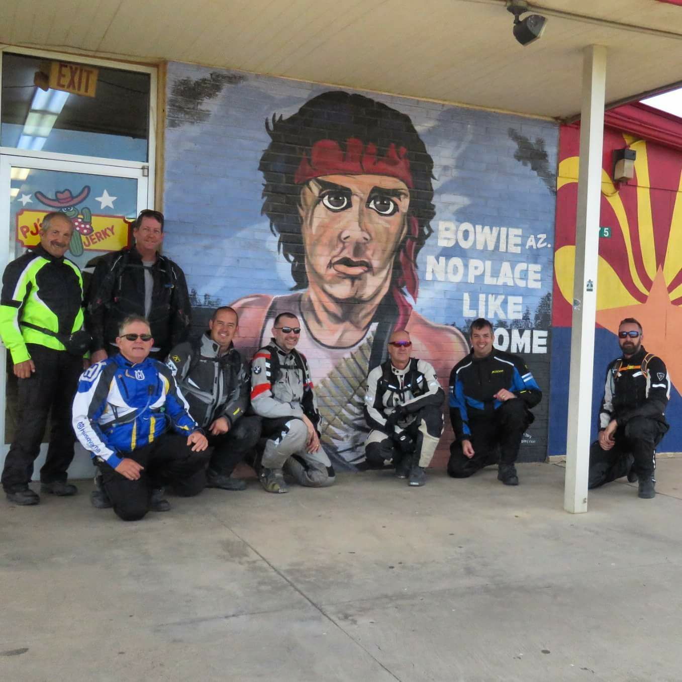 A group of men pose in front of a bowie mural