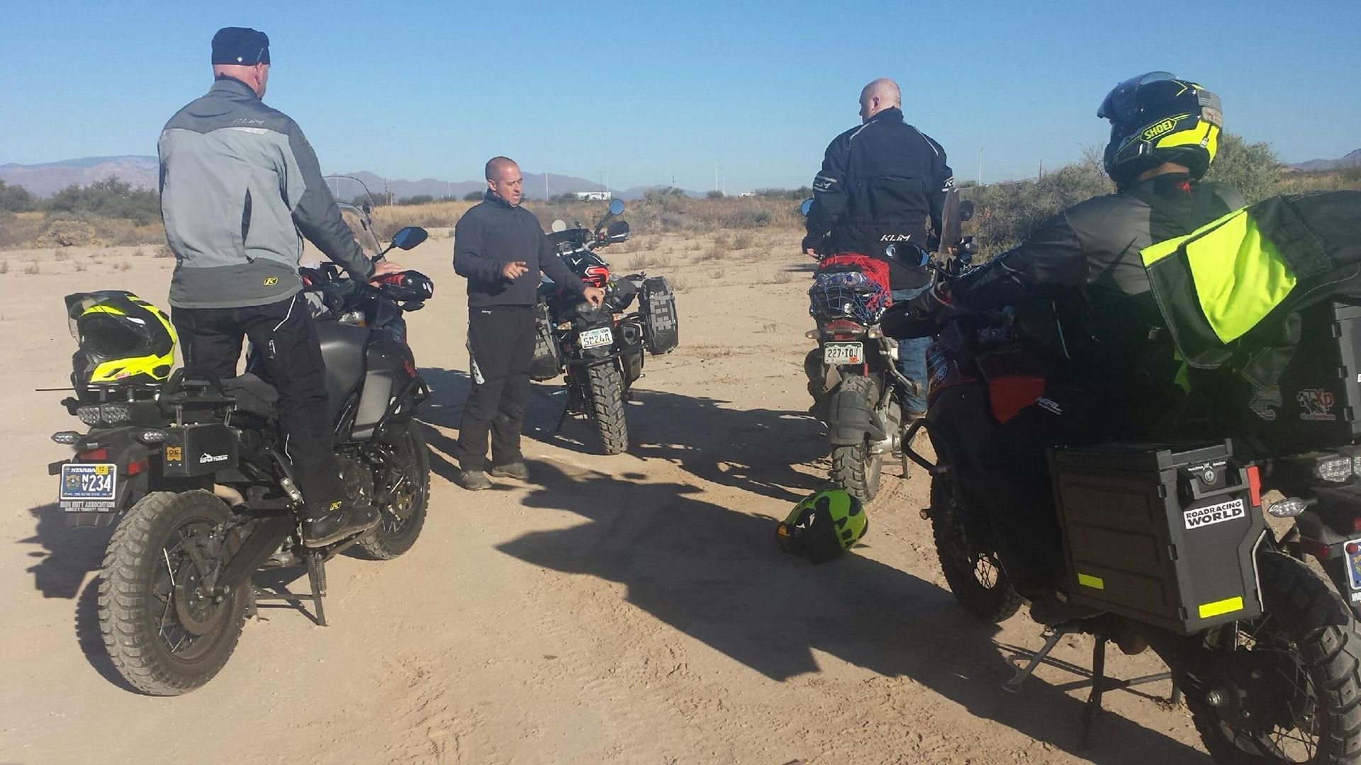 A group of men are standing next to motorcycles in the desert.