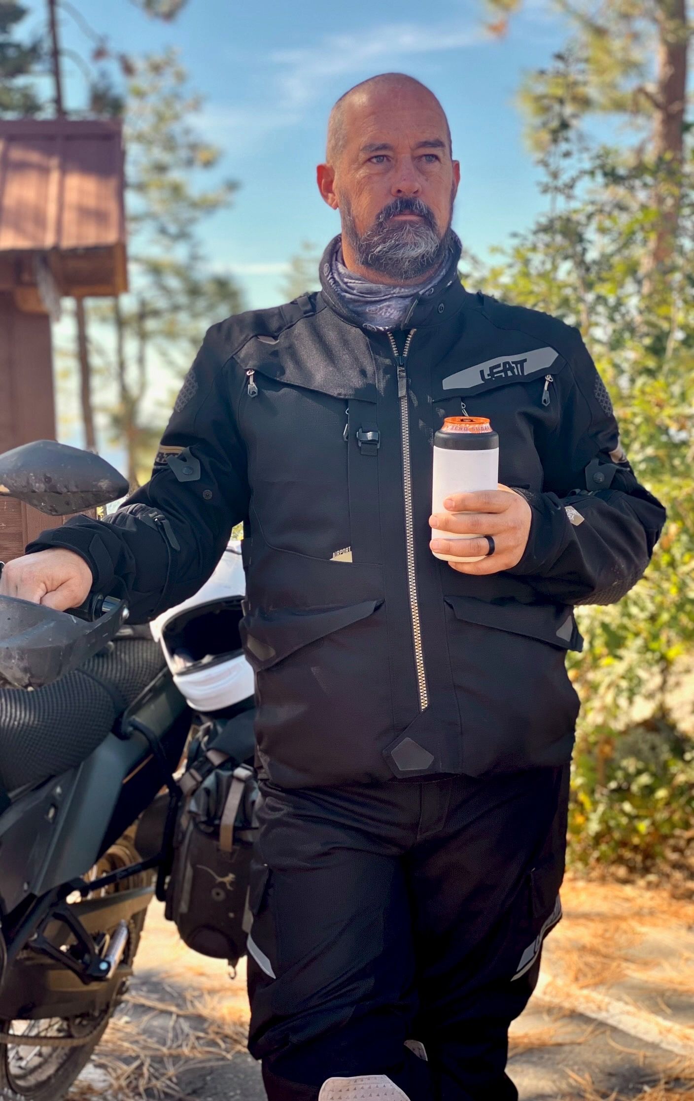 Torso of a man reaching into motorcycle bag with drink in his hand. 
