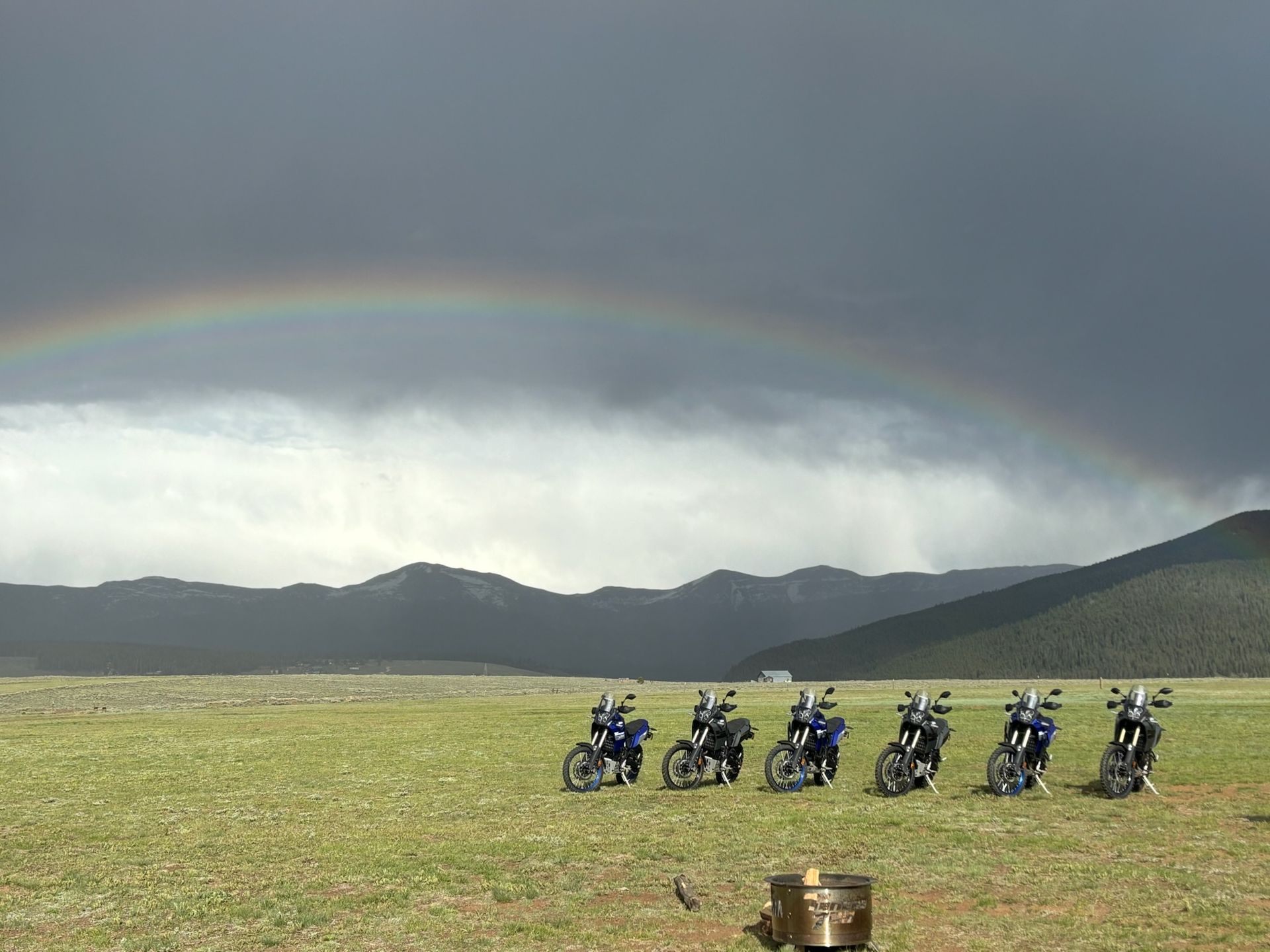 A group of motorcycles are parked in a field under a rainbow.