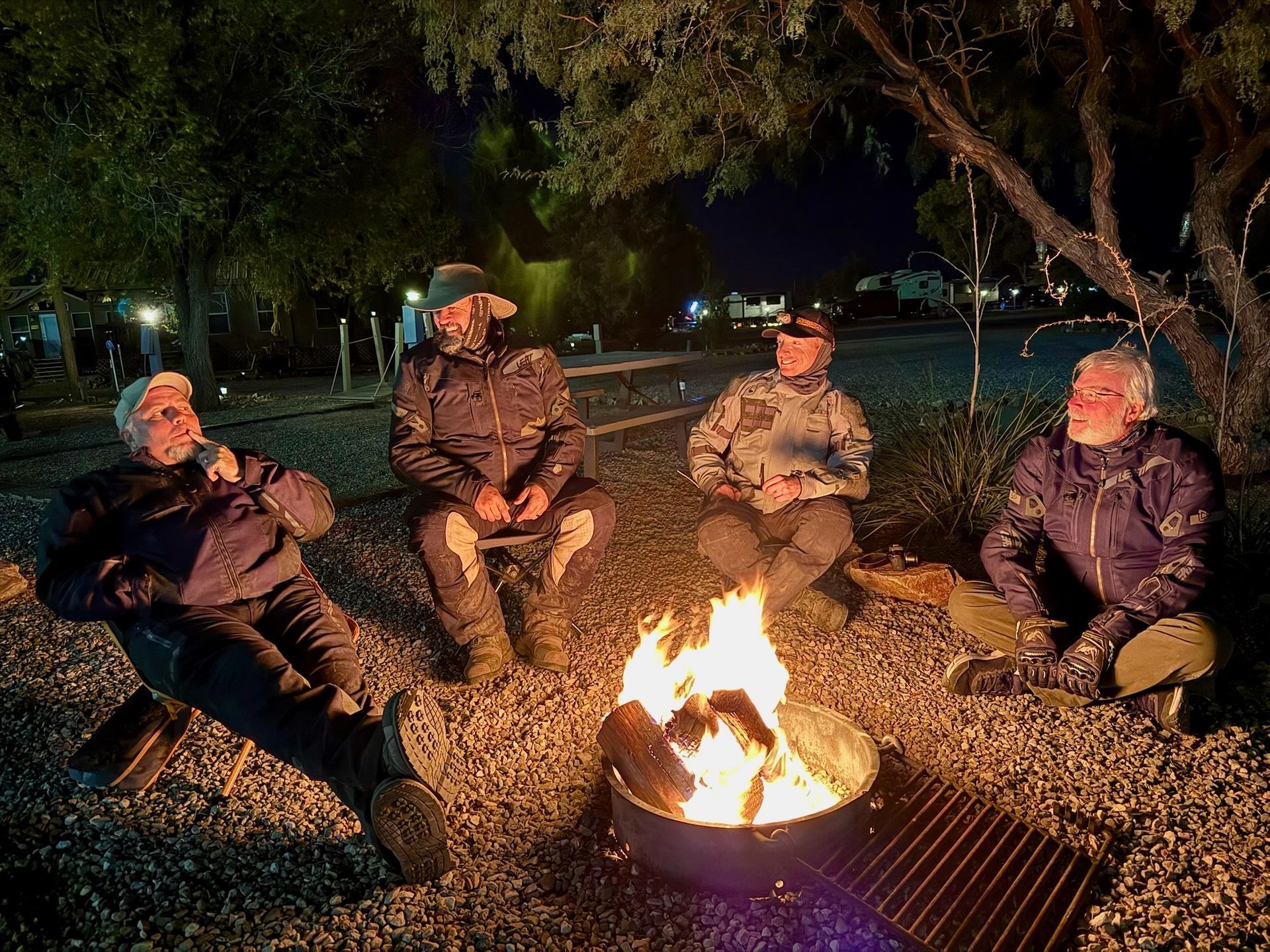 A group of people are sitting around a fire pit at night.