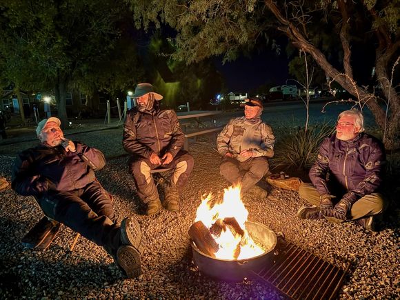 A group of people are sitting around a fire pit at night.