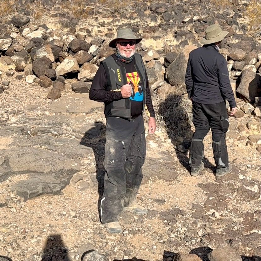 Picture of a man wearing a vest and riding pants in the desert with rocks.