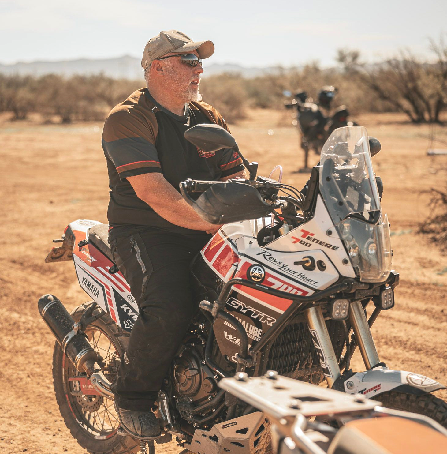 Man seated on a white and red adventure motorcycle in a desert setting.