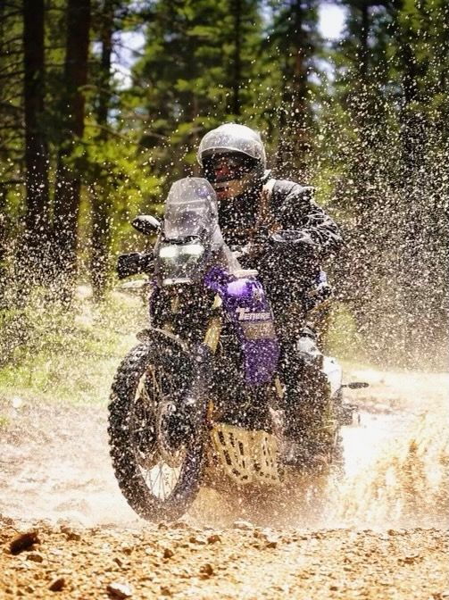 Photo of a person riding on a motorcycle through the water, splashing water in the air