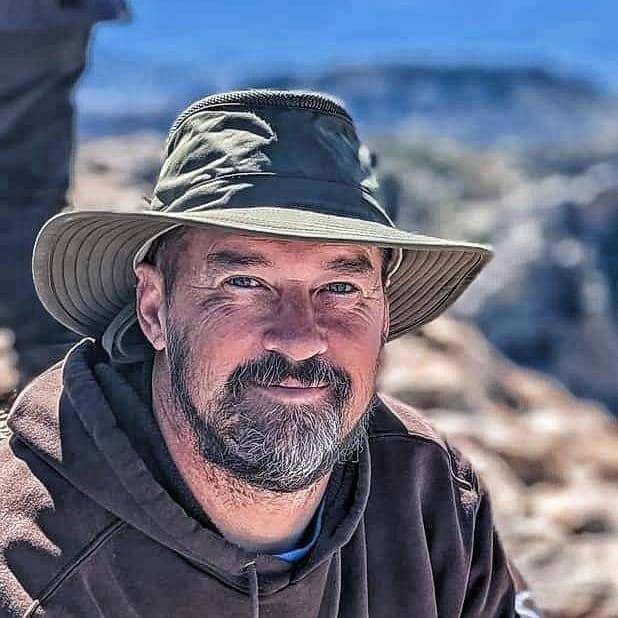 Close up photo of a man with a beard, and green hat. 