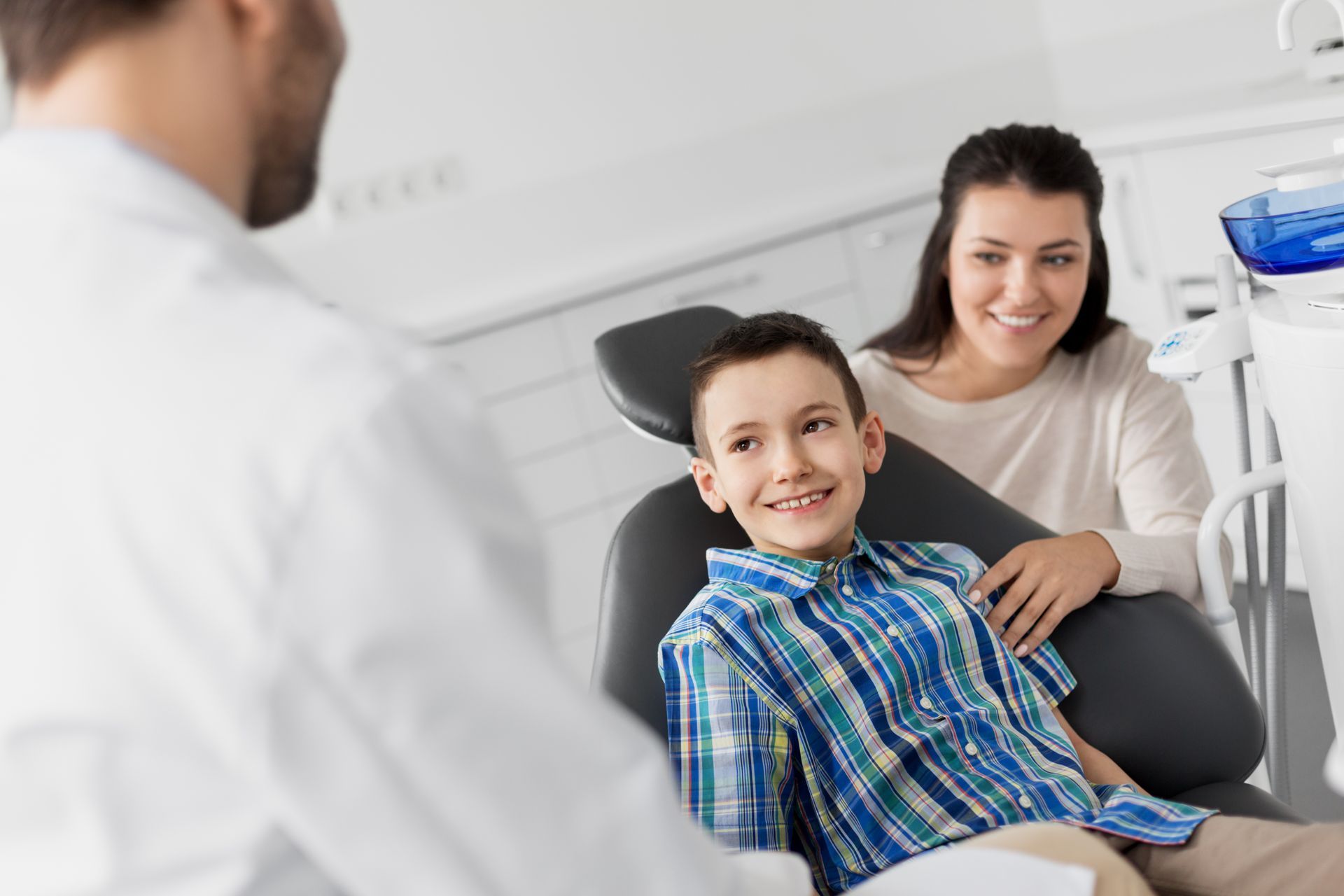 Child reclining in a dental chair while a dentist speaks, with an adult seated beside the chair.