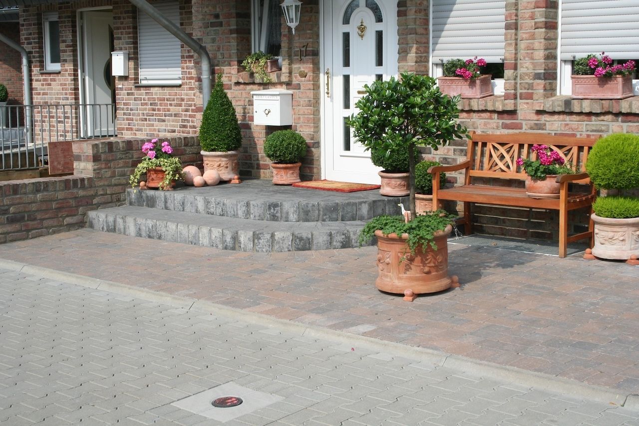 Vorgarten mit gepflastertem Weg und Stufen, umgeben von grünen Pflanzen und einer Holzbank zum Verweilen.