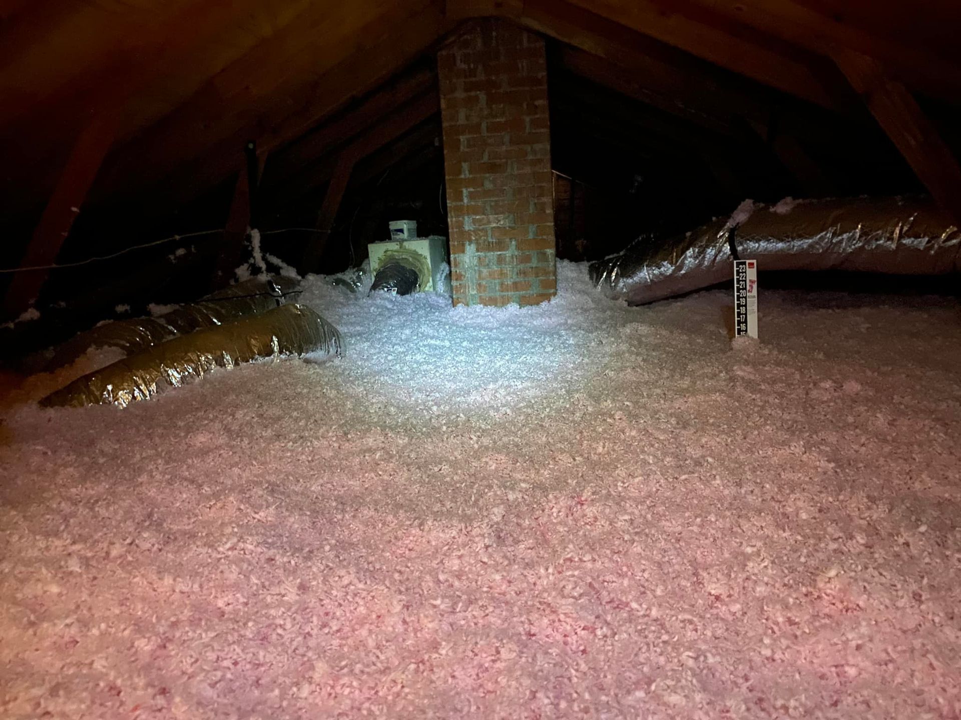 An attic filled with pink insulation and a brick chimney.