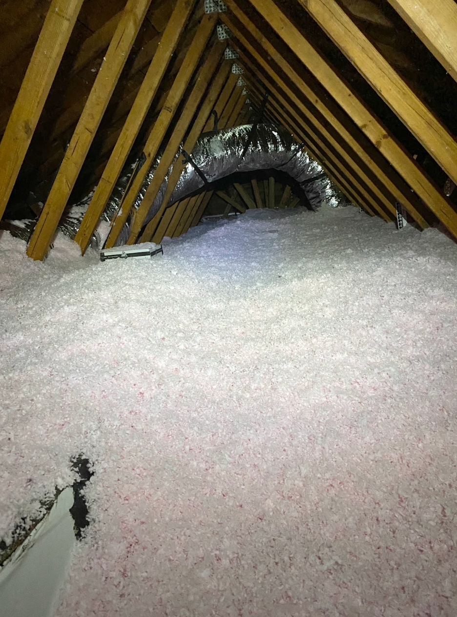 Attic with pink insulation filling the space, wooden beams overhead.