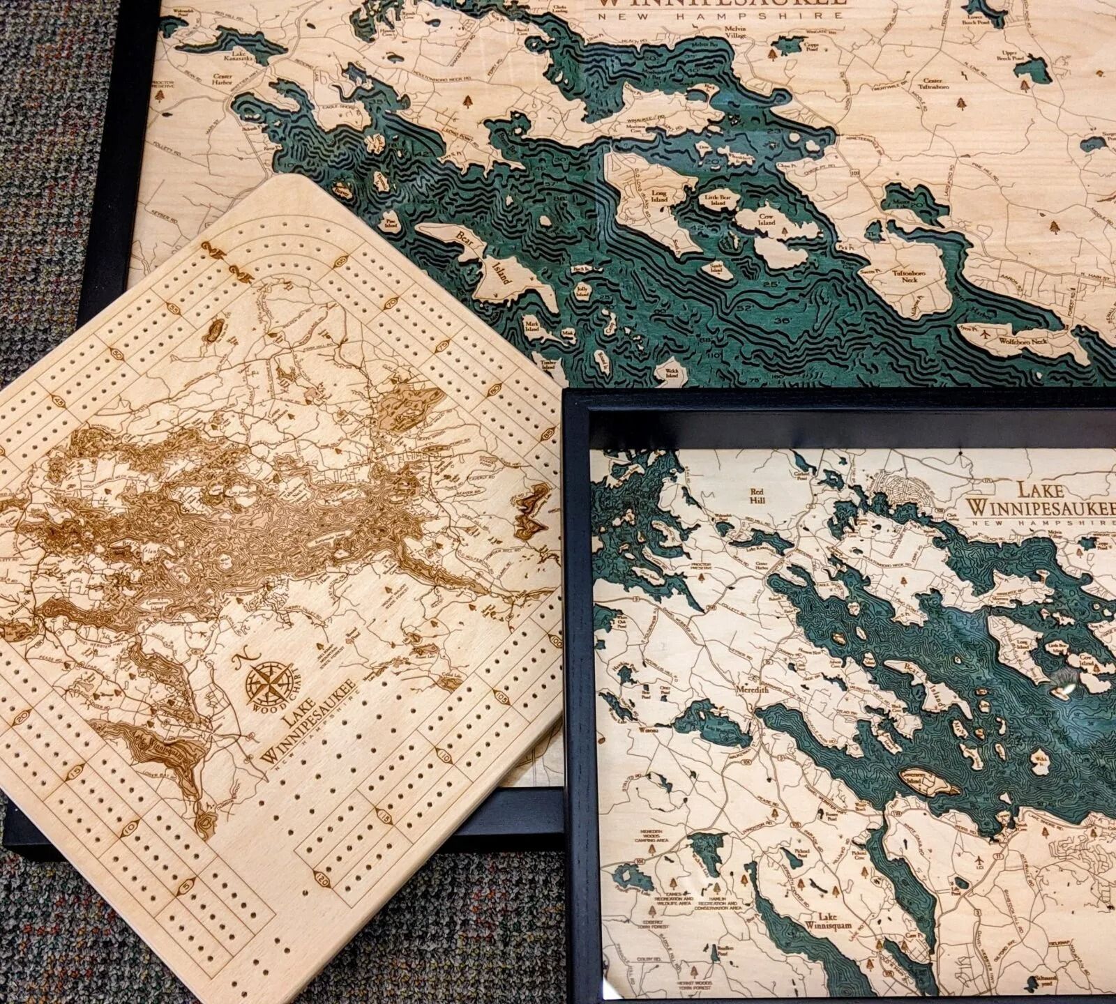 Three framed wooden maps with intricate details; one is a cribbage board.