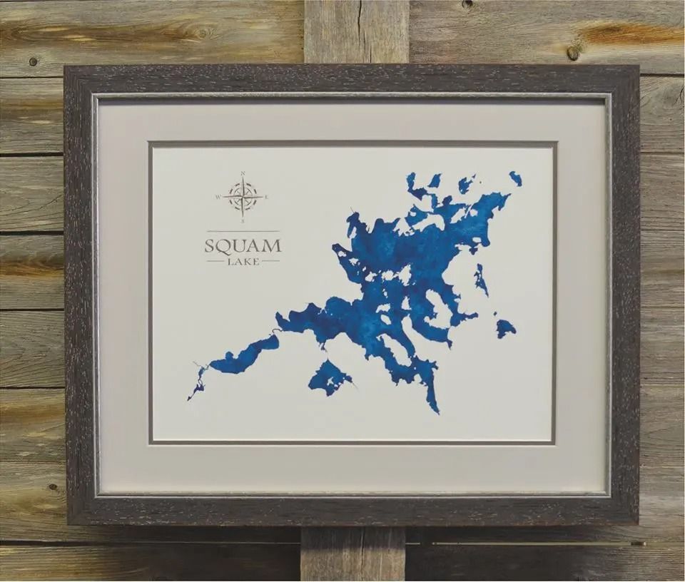 Framed map art of Squam Lake, New Hampshire. Blue watercolor lake on white matting, gray frame, compass rose.