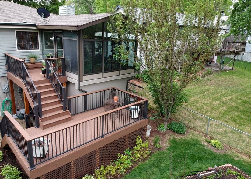 A multi-level deck attached to a house with a screened-in porch and stairs, in a grassy backyard.
