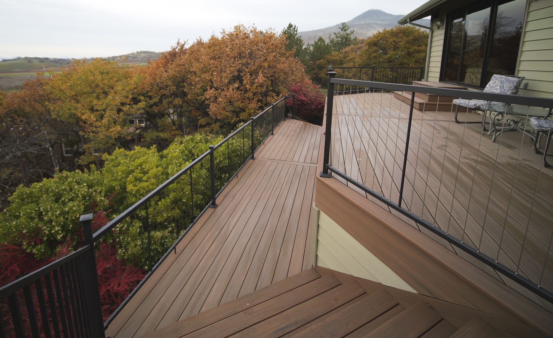 Wooden deck with black railings overlooks colorful trees in autumn.