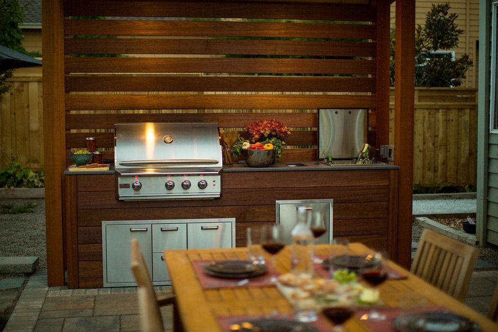 Outdoor kitchen with grill, prep space, and dining table, lit by warm light.
