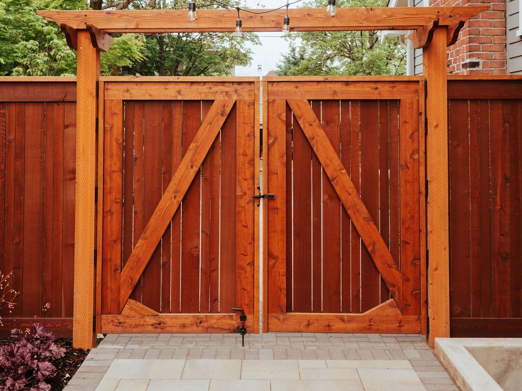 A wooden gate with a pergola attached to it is surrounded by a wooden fence.
