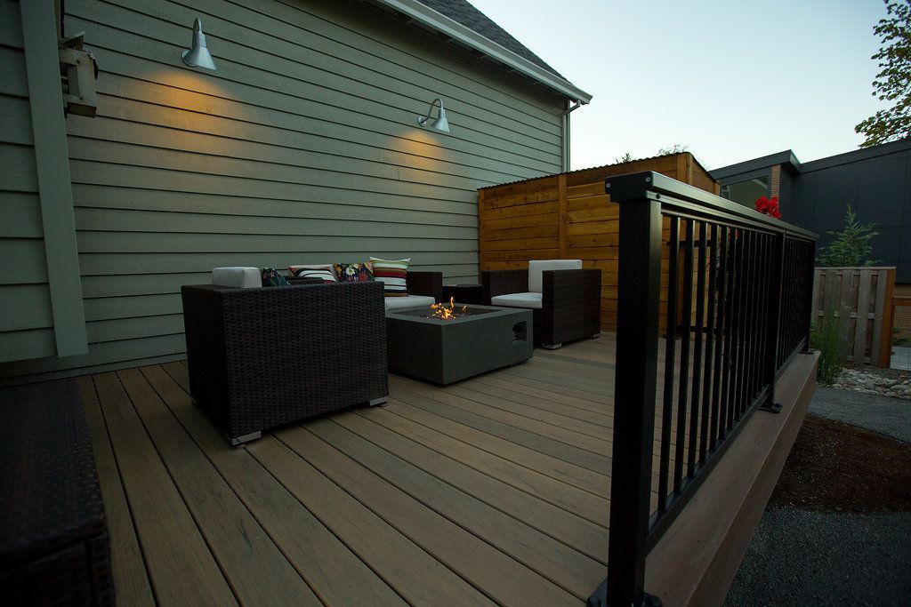 Outdoor deck with seating around a fire pit, against a wood-slatted wall, lit by sconces.