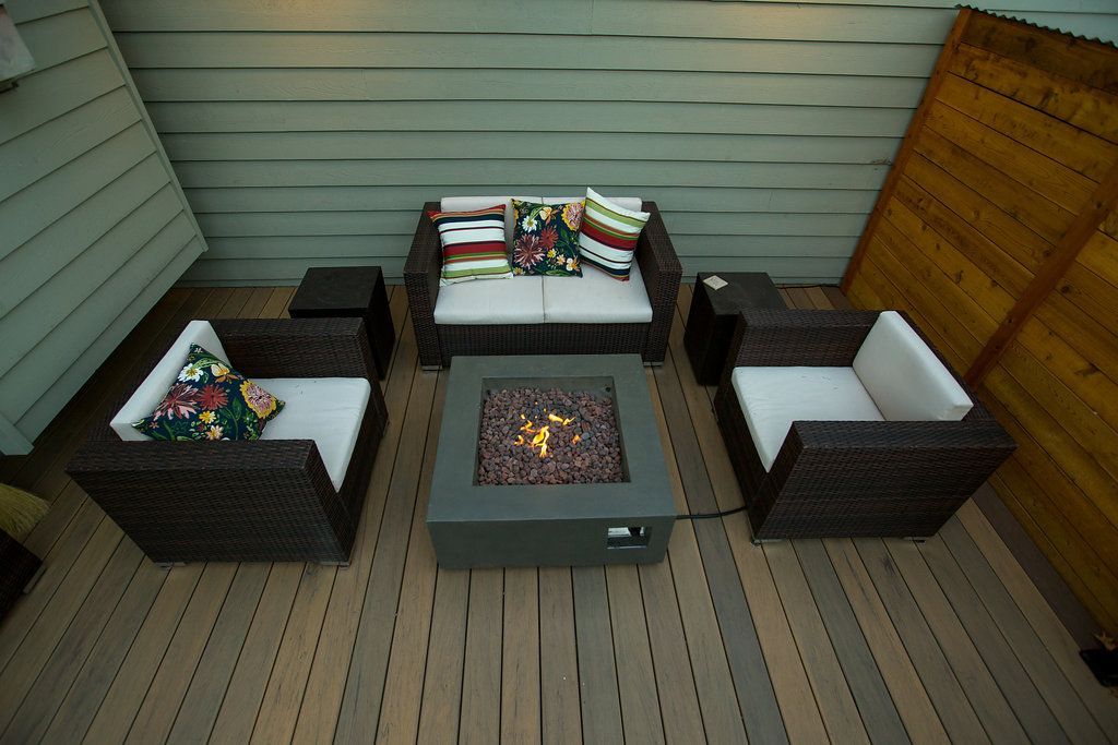 Outdoor patio furniture with a fire pit. Brown wicker seating with white cushions.