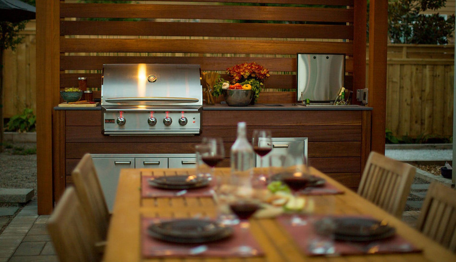 There is a table with plates and wine glasses on it and a grill in the background.