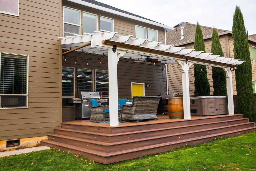 Backyard patio with pergola, seating, built-in grill, hot tub, and grass lawn.