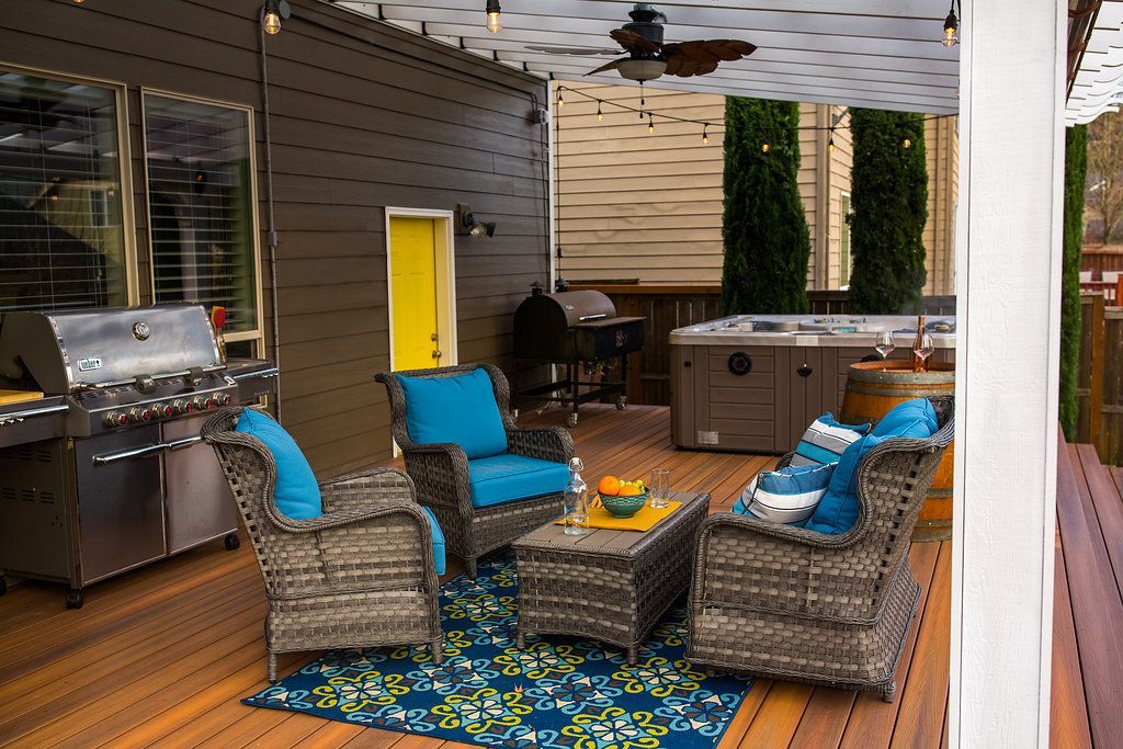 Patio with grill, wicker furniture, hot tub, and string lights. Turquoise cushions and a blue rug.