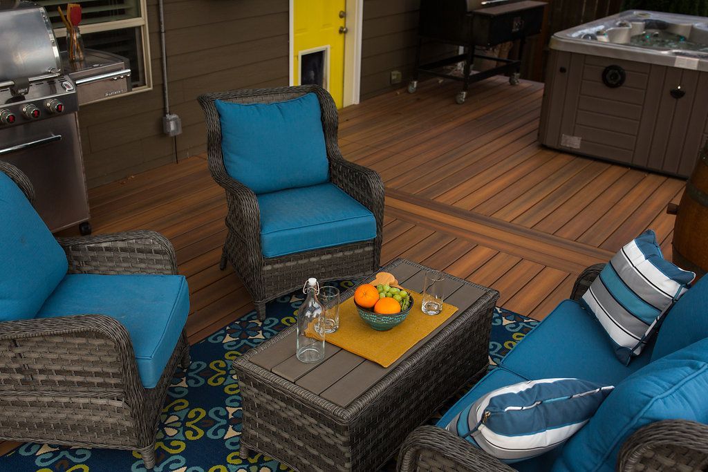 Outdoor patio with teal cushions, seating set, coffee table, and hot tub.