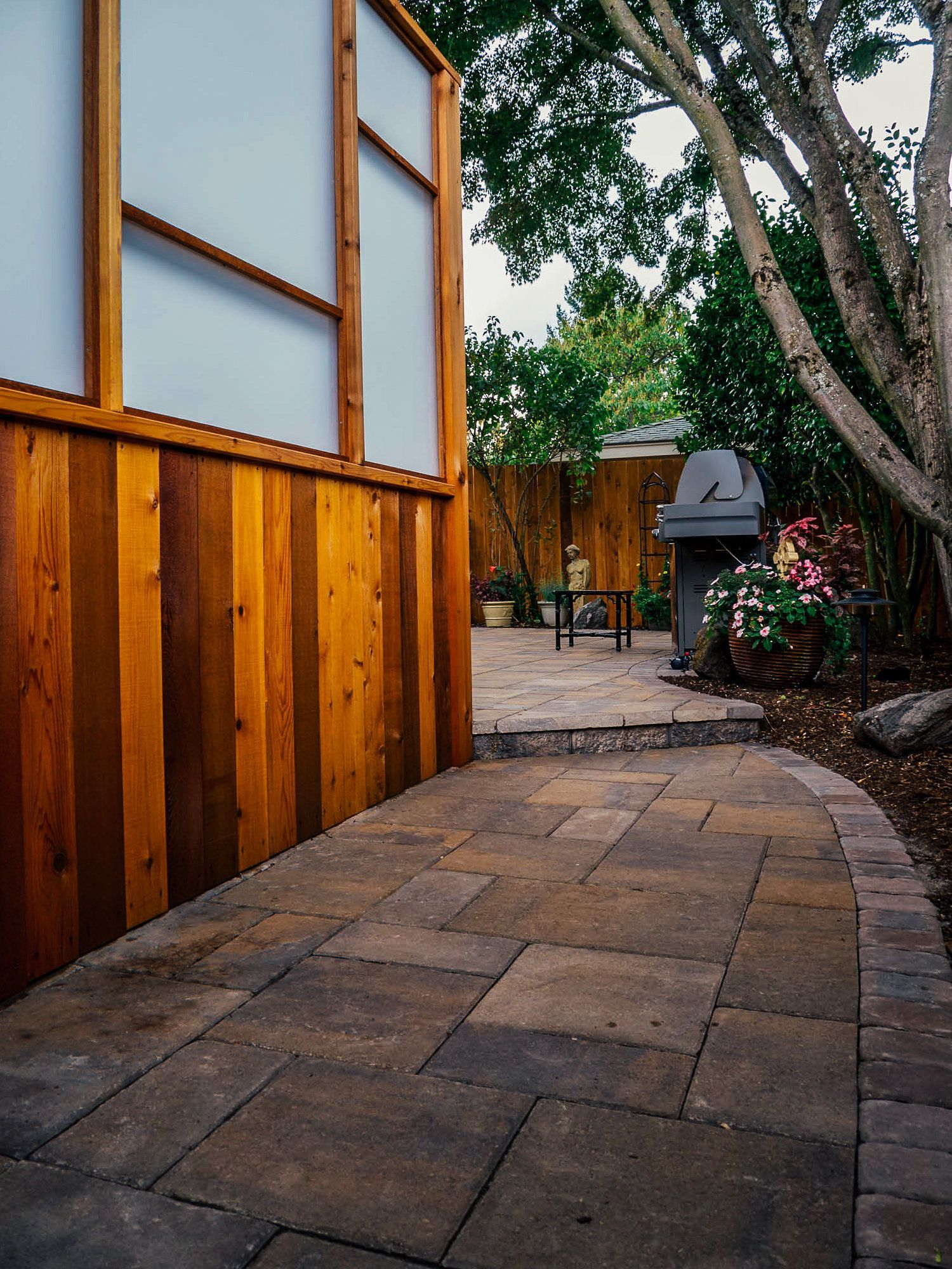 A walkway leading to a patio with a wooden fence and a grill.
