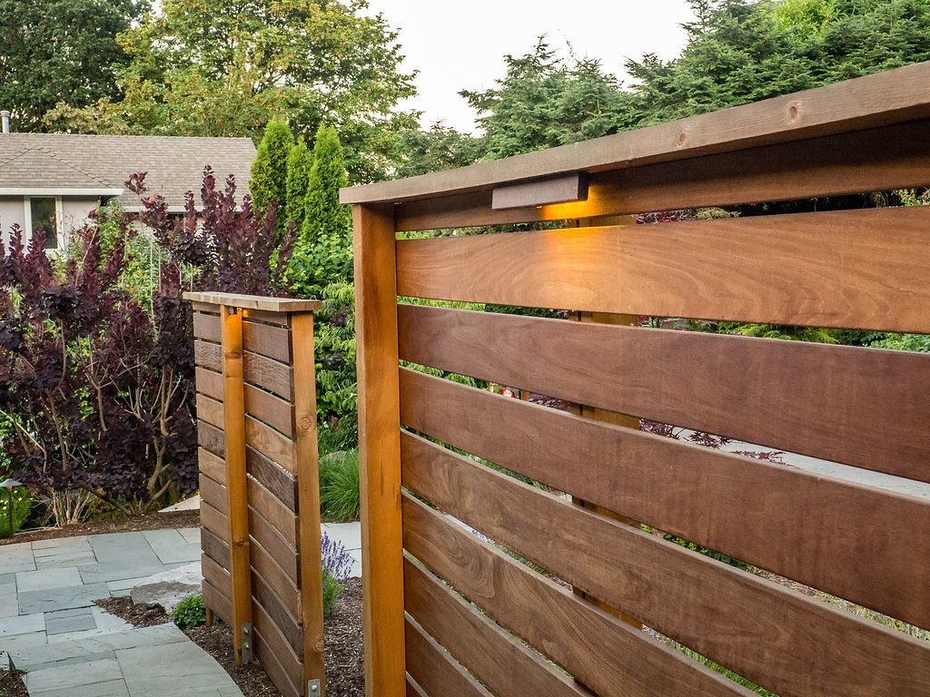 A wooden fence is surrounded by trees and bushes in a backyard.