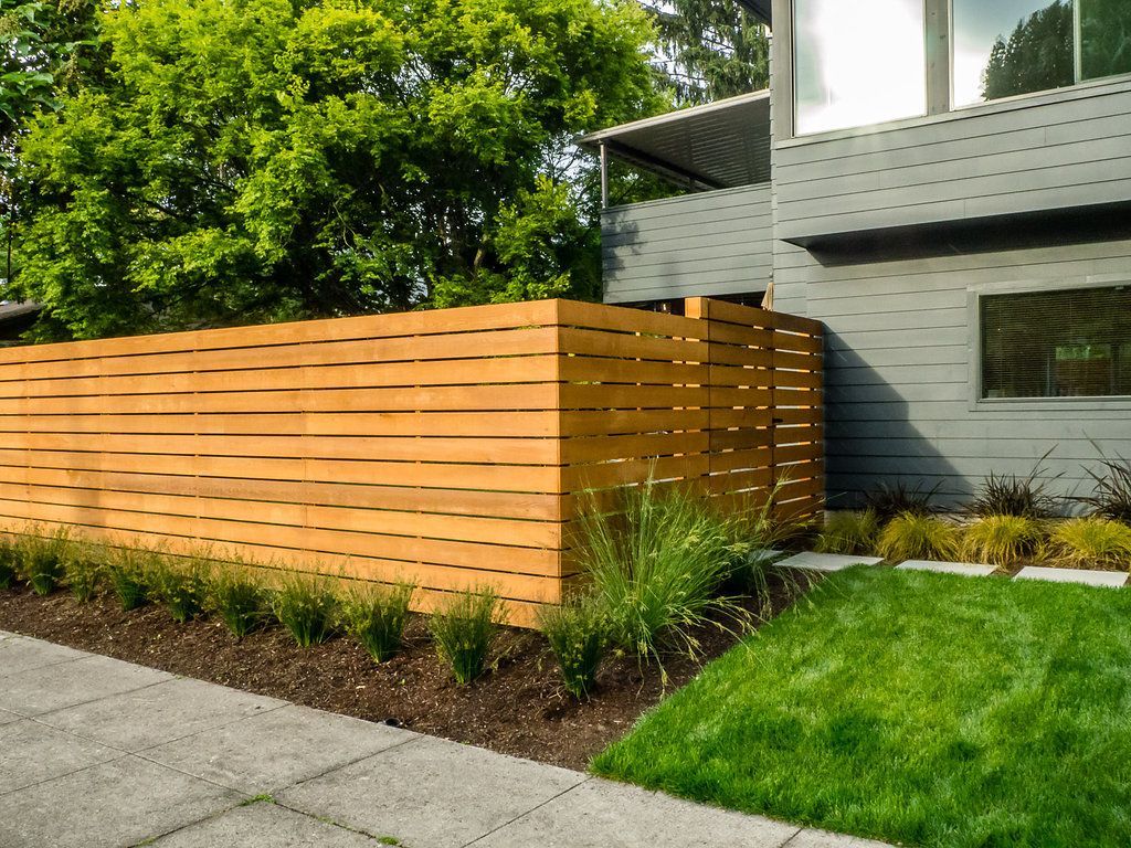 A wooden fence surrounds a lush green lawn in front of a house.