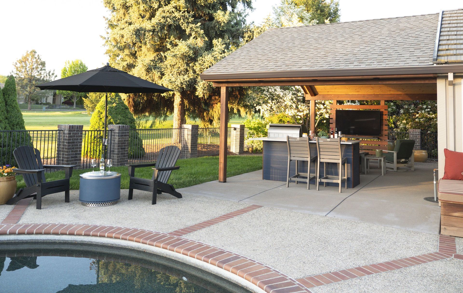 Outdoor patio with pool, umbrella, bar, seating, and views of a golf course.