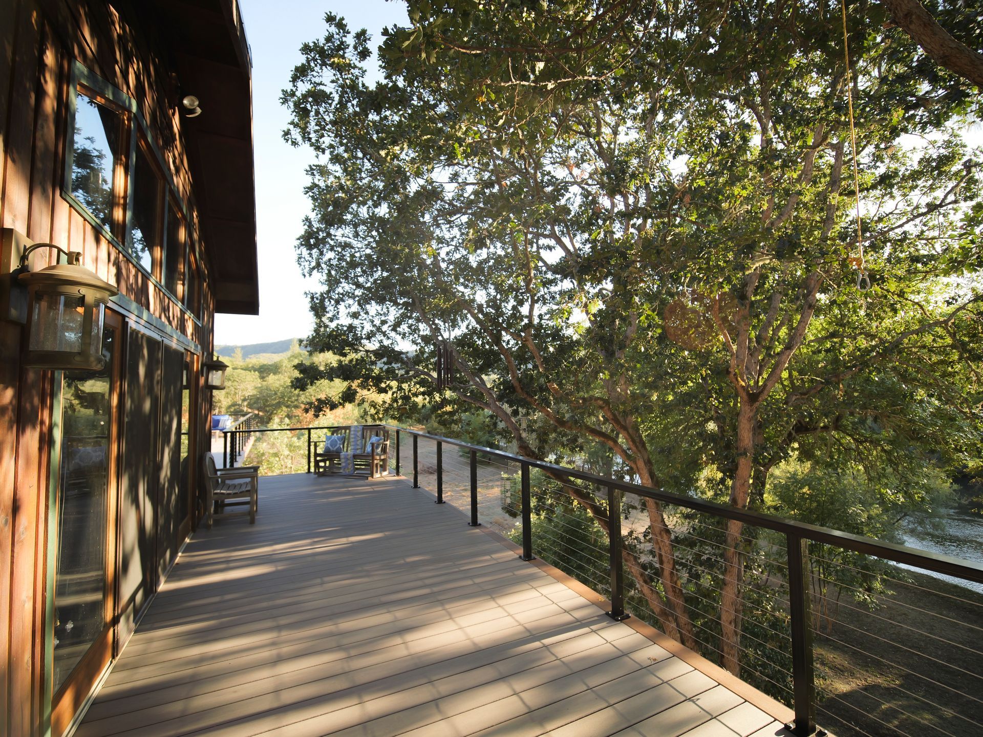 Wooden deck with black railing overlooking trees and a distant landscape.