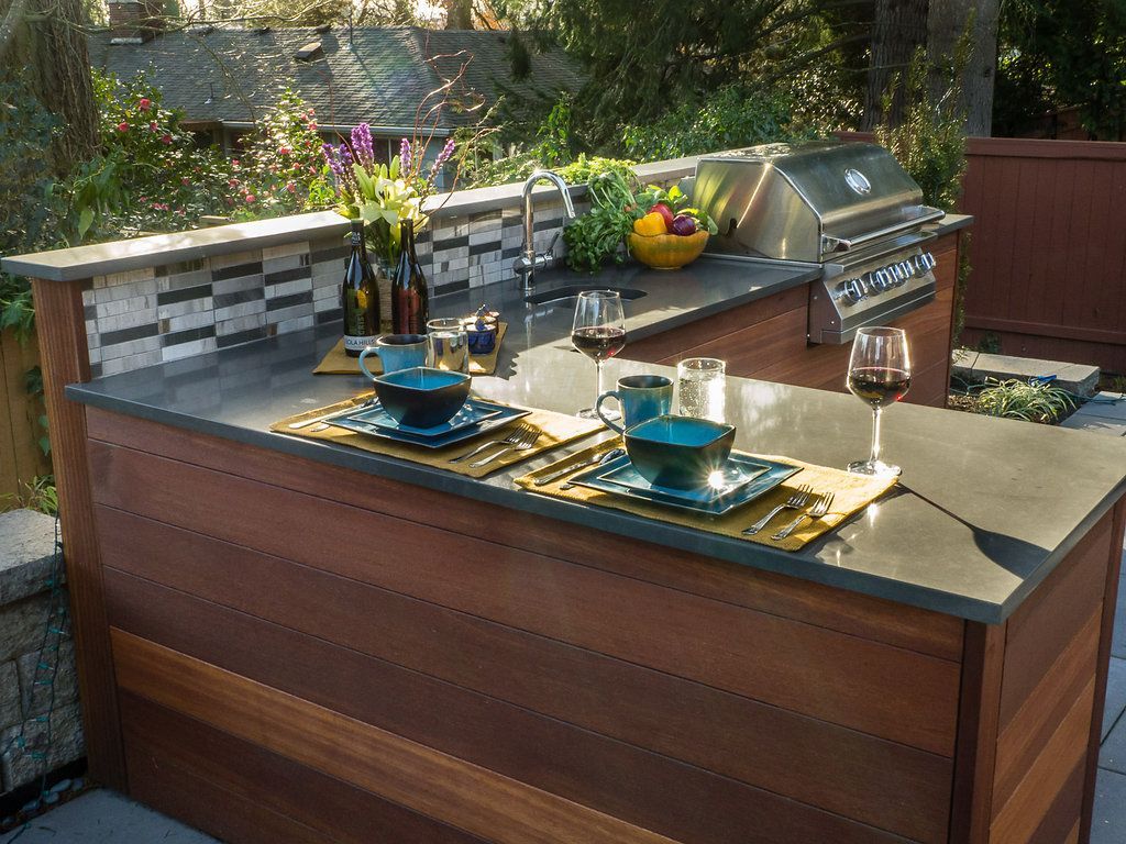 Outdoor kitchen with grill, sink, and countertops set for dining.