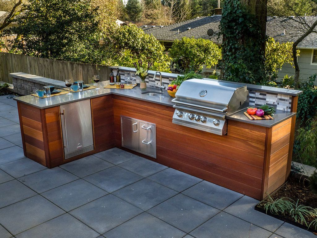Outdoor kitchen with stainless steel appliances, wood cabinets, and gray stone patio.