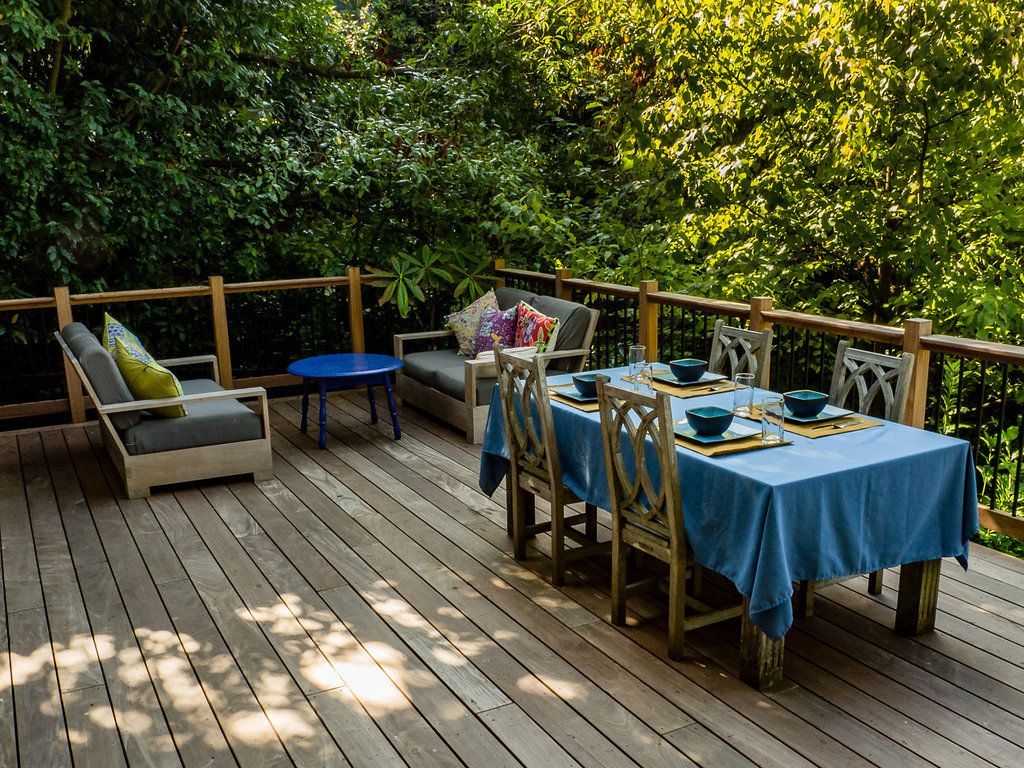 Wooden deck with outdoor furniture, dining table set for a meal, surrounded by trees.