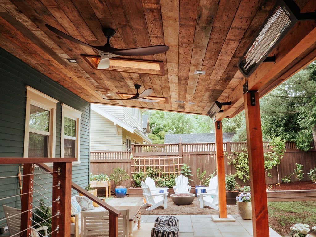 Covered patio with wooden ceiling, fans, heaters. View of backyard with seating and fire pit.