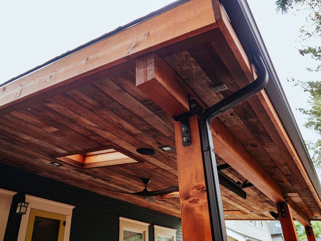 Wooden porch with dark gutter, ceiling fan, and skylight, attached to a dark green house.