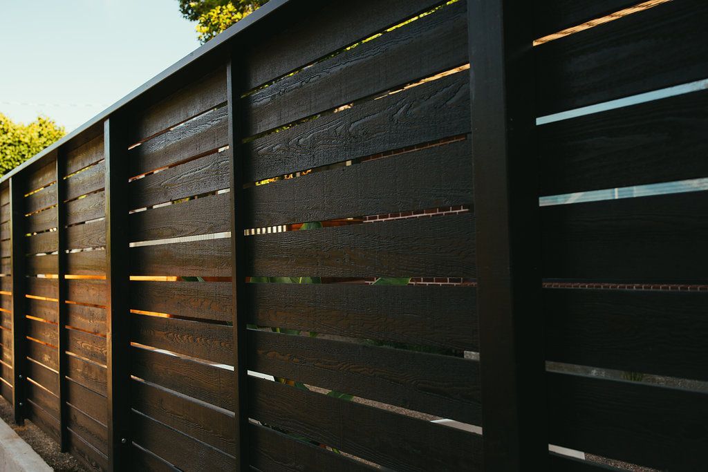 A close up of a black wooden fence with trees in the background.