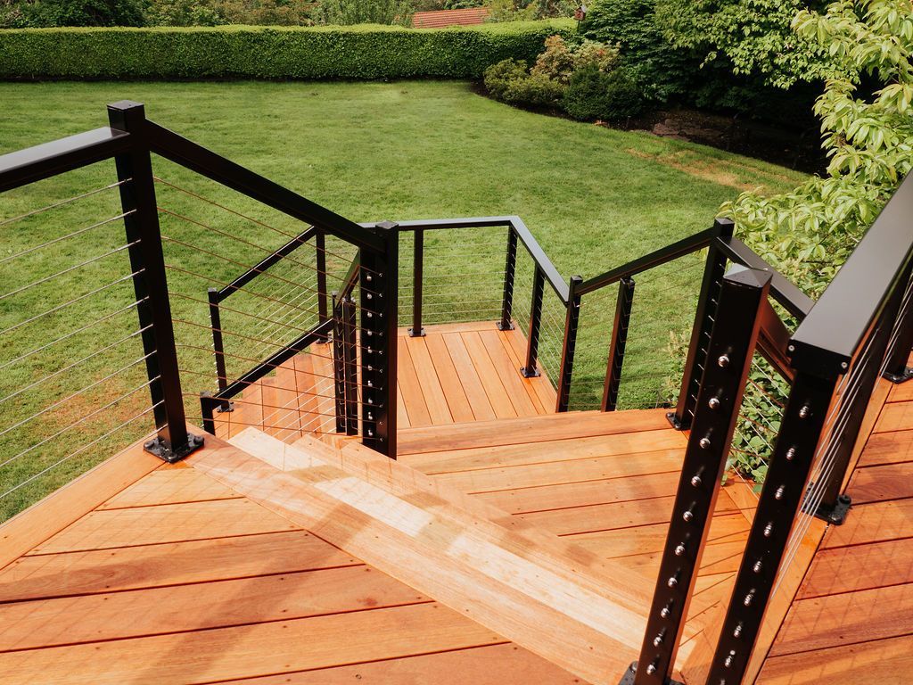 Wooden deck with black railing, descending stairs, overlooking a green yard.
