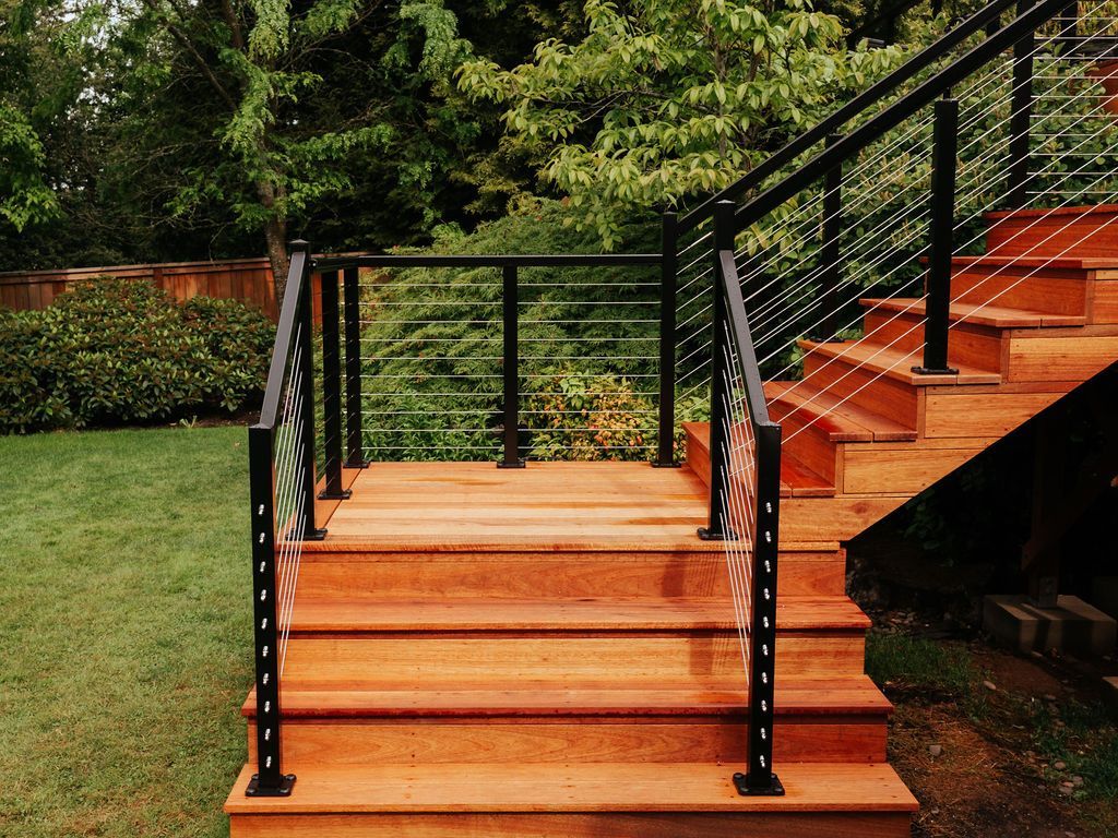 Wooden outdoor staircase with black metal railing, lush green yard and trees.