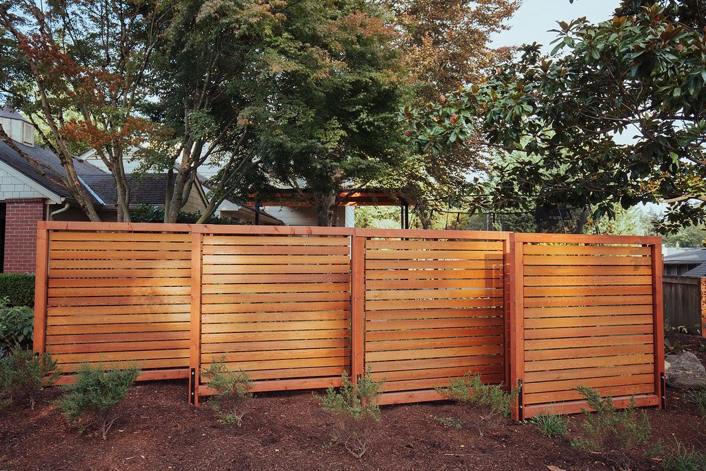 A wooden fence is surrounded by trees in front of a house.
