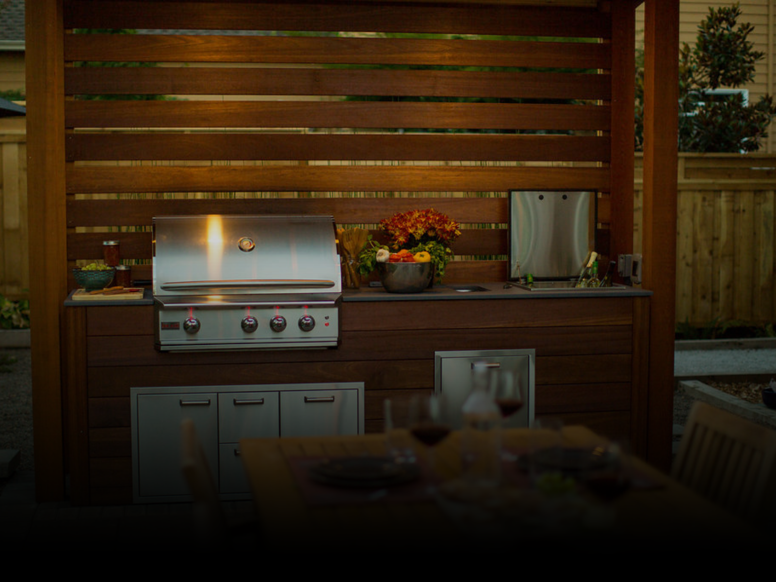 An outdoor kitchen with a grill and a table with plates and wine glasses.