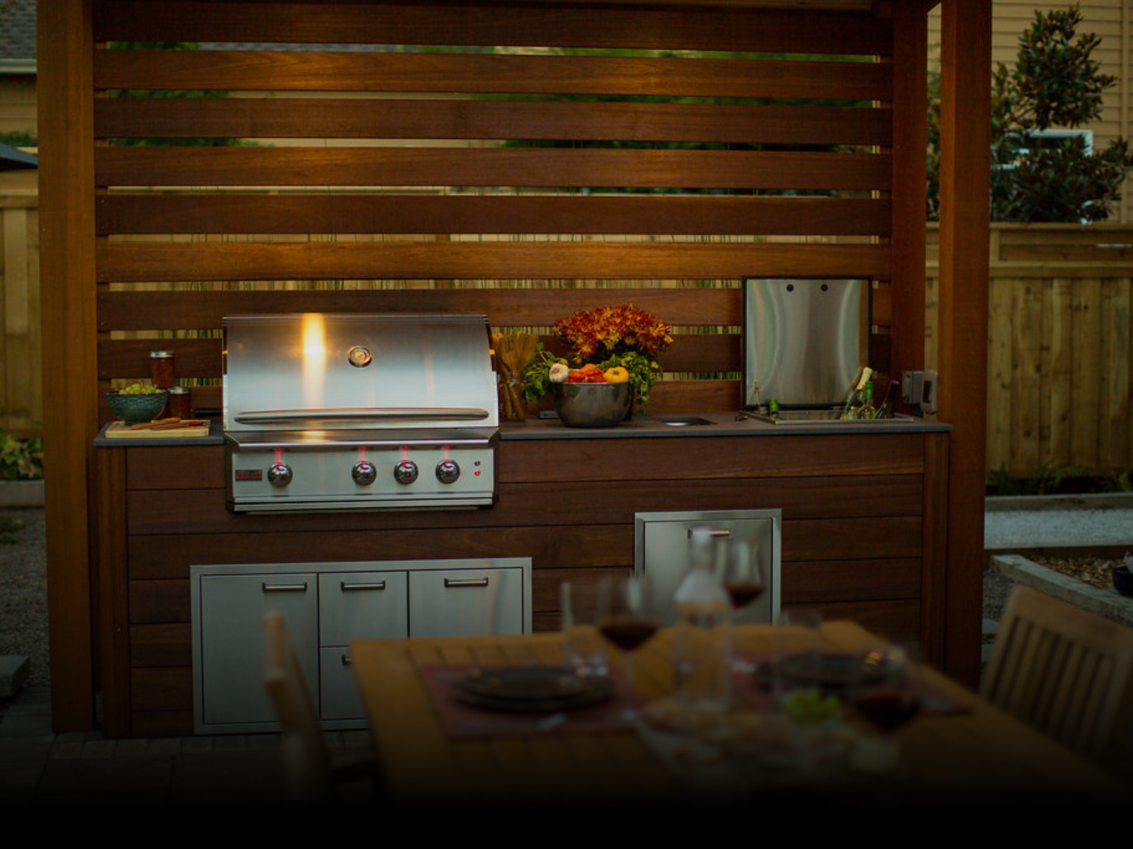An outdoor kitchen with a grill and a table with plates and wine glasses.