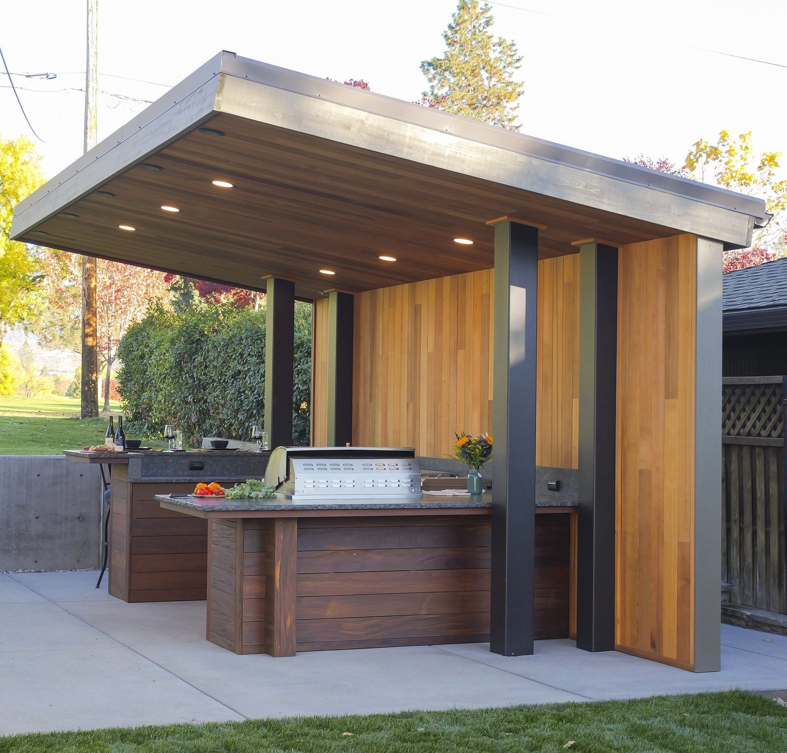Outdoor kitchen with wood features, including a grill and bar area under a covered structure.