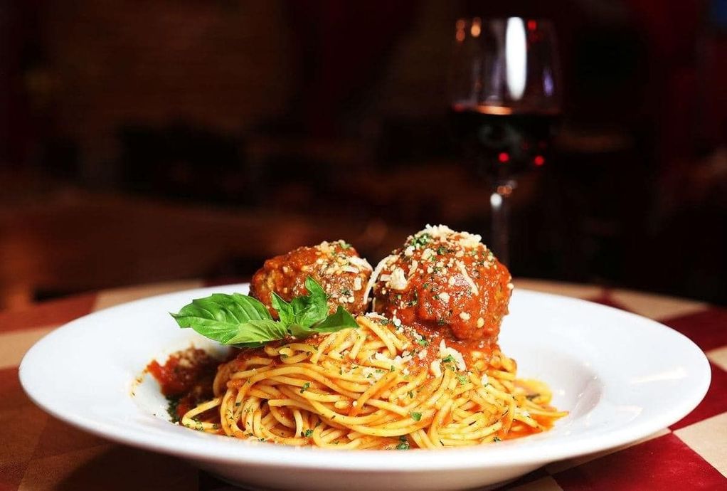 A plate of spaghetti and meatballs with a glass of wine in the background.