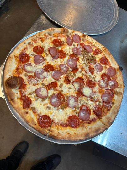 A pizza with pepperoni and sausage on a pan on a table.