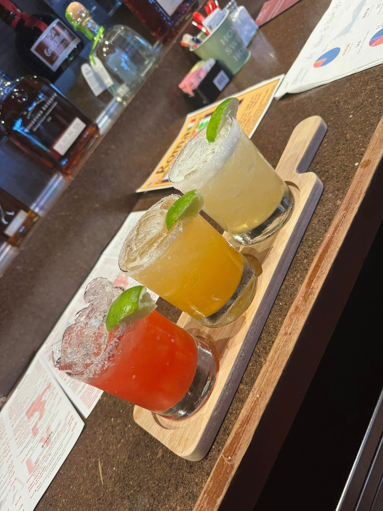 Three different colored drinks are on a wooden tray on a table.