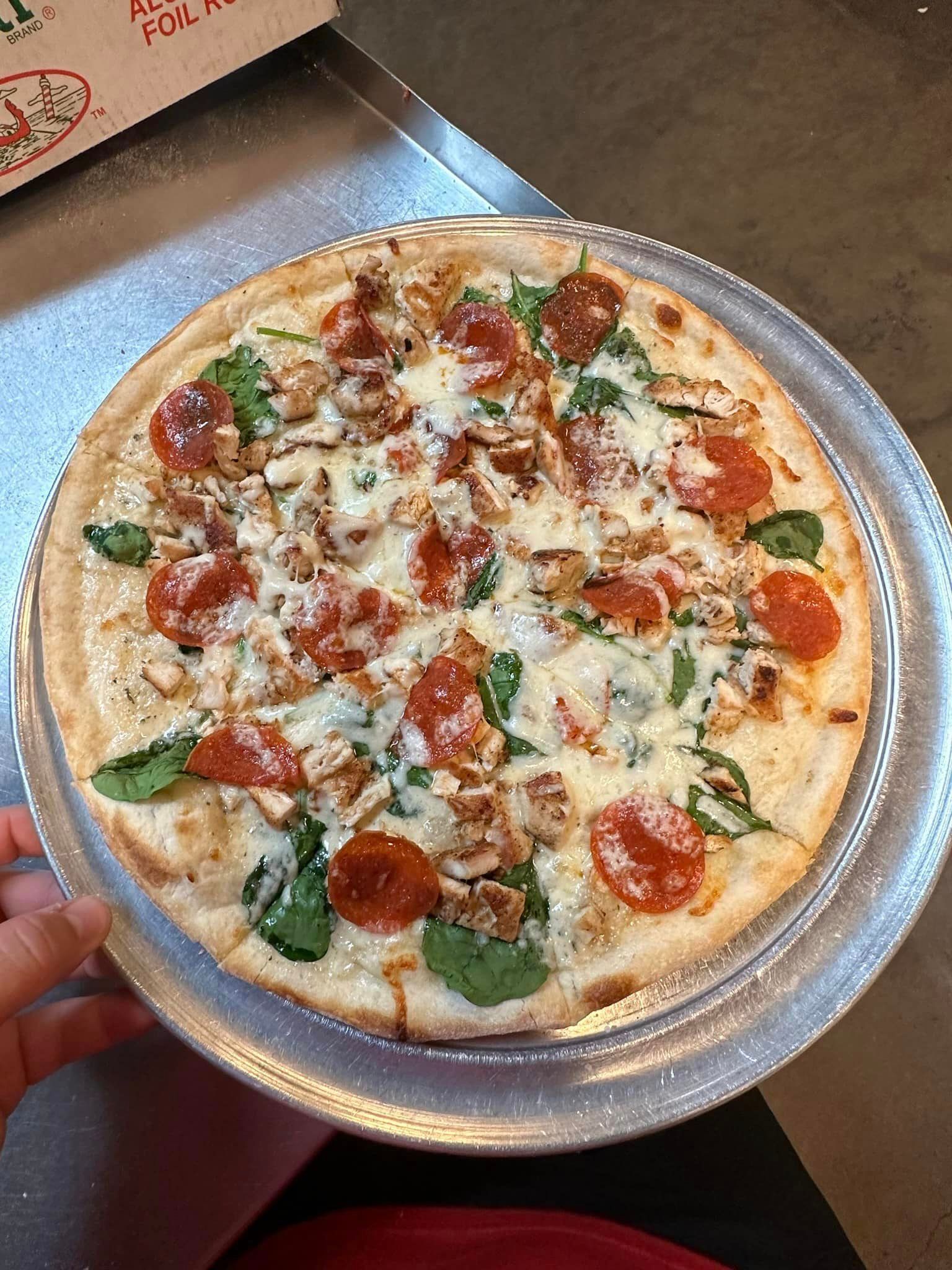 A pizza with pepperoni , spinach , mushrooms and cheese on a silver plate.